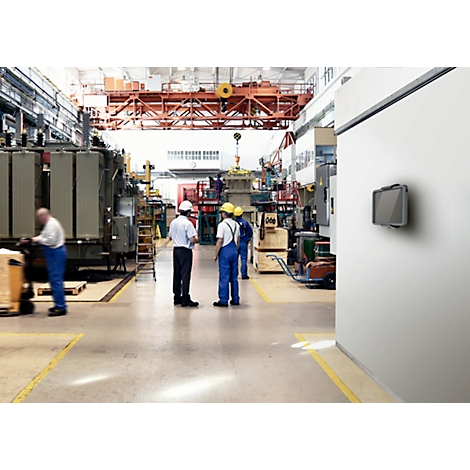 Factory workers working on a machine. A screen on the wall. Yellow markings on the floor.