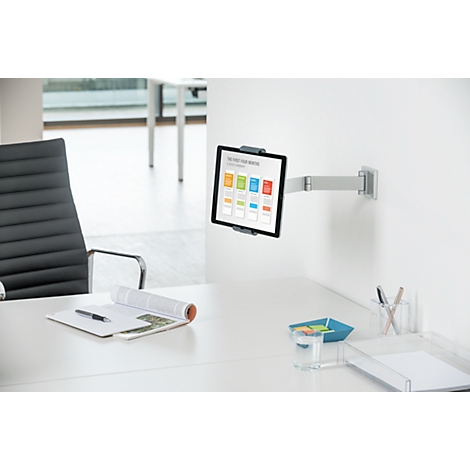 Tablet on wall mount, notes, pens, a blue bowl and a glass of water on the desk.