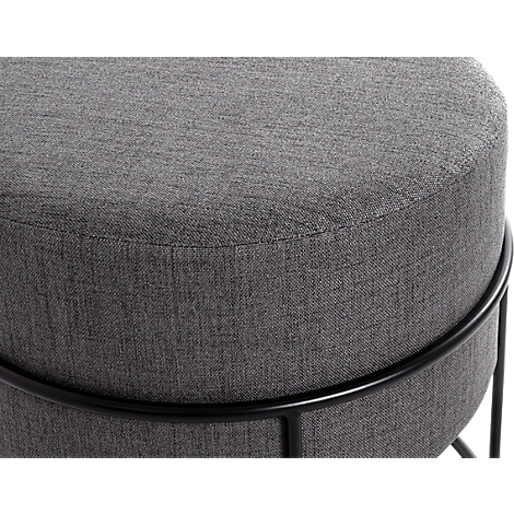 Gros plan d'un tabouret rond gris avec un cadre en métal noir. La surface est en tissu.