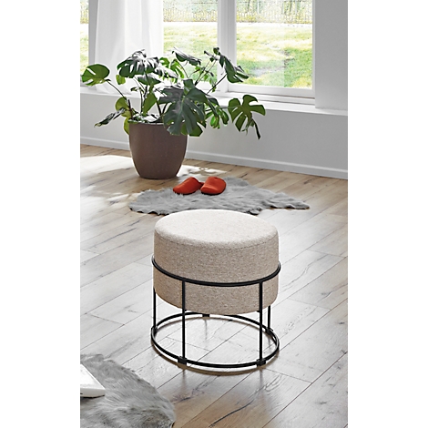 Tabouret rond avec revêtement en tissu beige et structure en métal noir. Une plante et des chaussures rouges en arrière-plan.