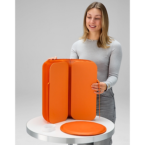 Une femme tenant un meuble orange pliable sur une table.