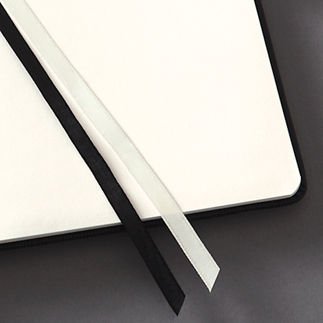 Nahaufnahme eines offenen Notizbuchs mit schwarzem und weißem Leseband auf hellen Seiten. Grauer Hintergrund.