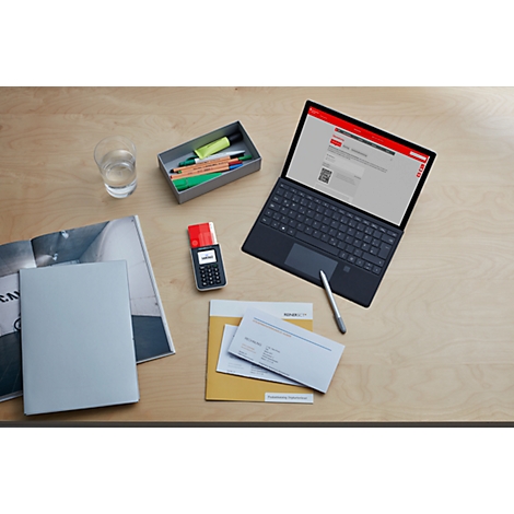 Draufsicht: Laptop, Stift, Kartenlesegerät, Briefe auf Holztisch. Auf dem Laptop ein rotes Banner.