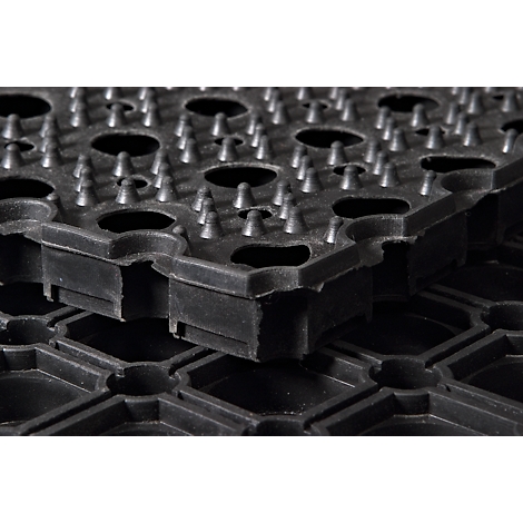 Gros plan d'un tapis en caoutchouc noir avec des clous et des ouvertures hexagonales. Deux tapis sont empilés.