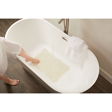 Un pied touche un tapis de bain antidérapant dans une baignoire où l'eau coule du robinet.