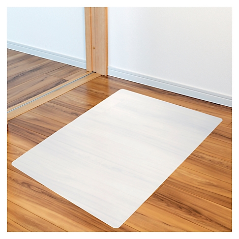 Tapis de protection de sol transparent rectangulaire sur un sol en bois. Derrière, un mur blanc et un cadre de porte.