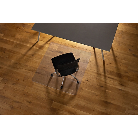 Chaise de bureau sur un tapis de protection de sol transparent sous un bureau gris sur un plancher en bois. Ombre.