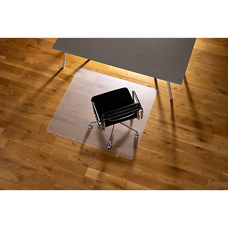 Chaise de bureau sur tapis de protection de sol transparent sous un bureau sur plancher en bois.