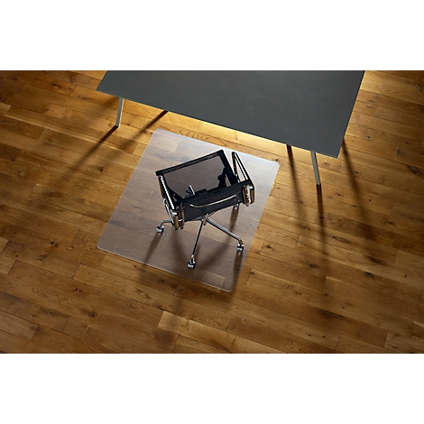 Chaise de bureau sur un tapis de sol transparent devant un bureau sombre. Le sol est en bois.