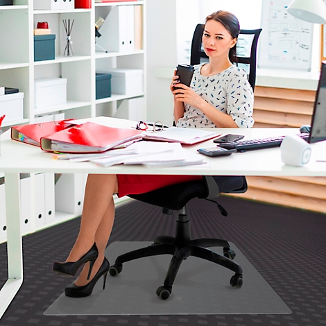 Femme au bureau, buvant du café. Sur le sol : tapis de chaise de bureau transparent. Jupe rouge, talons noirs.