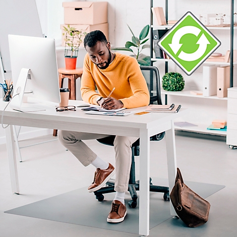 Un homme en pull jaune est assis à un bureau et écrit. Sur le bureau, un ordinateur, une tasse à café et des notes.