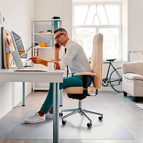 Un homme en chemise est au téléphone et pointe vers un ordinateur portable. Il est assis à un bureau avec une chaise dans un bureau lumineux.