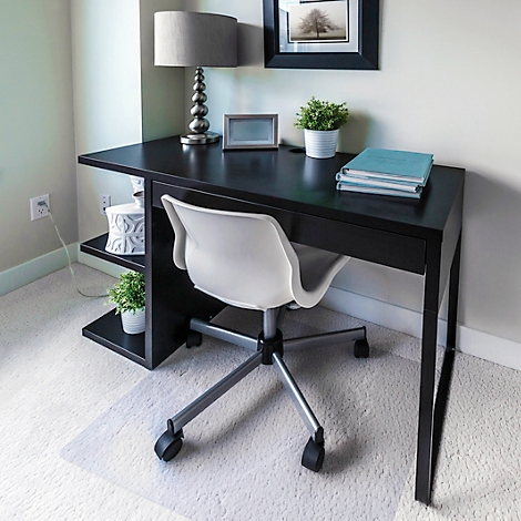 Bureau avec chaise de bureau, lampe, livres et décoration. Le tapis est clair, le mur est gris clair.