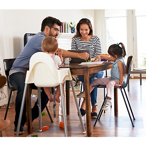 Une famille est assise à une table en bois; le père travaille sur un ordinateur portable, la mère et deux enfants regardent.
