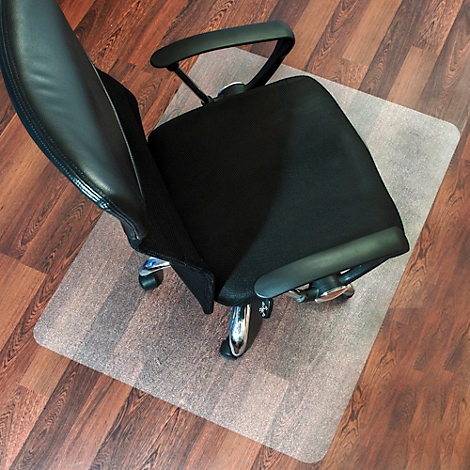 Chaise de bureau sur tapis de protection de sol transparent sur parquet. La chaise est noire, le tapis rectangulaire.