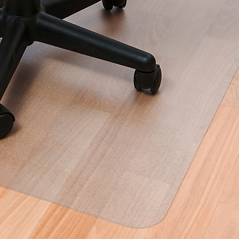 Tapis de protection de sol transparent sous une chaise de bureau, découpe d'angle, plancher en bois visible.