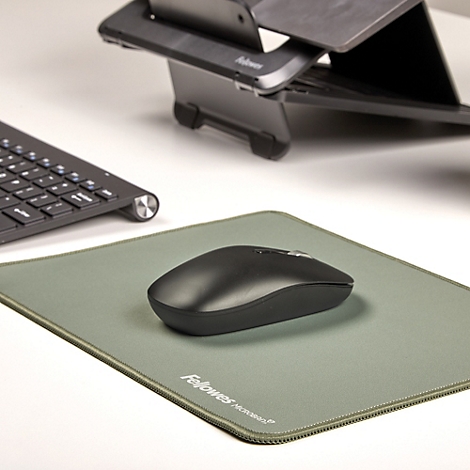 Une souris d'ordinateur noire est sur un tapis de souris vert à côté d'un clavier et d'un support pour ordinateur portable.