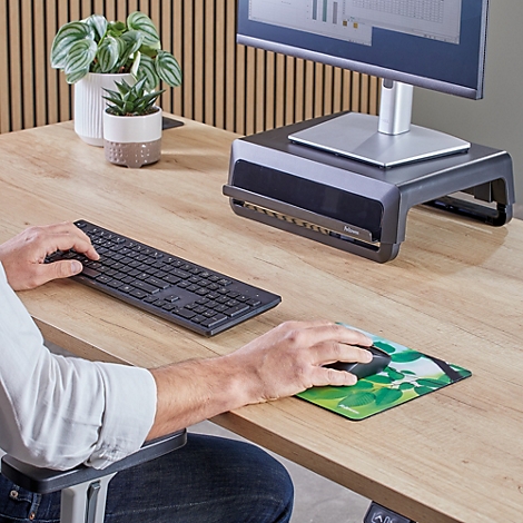 Tapis de souris rectangulaire avec un motif de feuilles dans des tons verts et jaunes. Logo Fellowes en bas à droite.