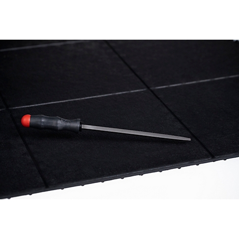 Une lime en métal avec un manche noir et un capuchon rouge est posée à plat sur un tapis de sol noir quadrillé.