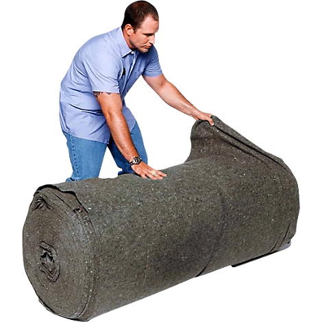 Un homme roule une couverture grise, la couverture est grande et lourde.