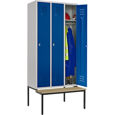 Armario azul y blanco con puerta abierta, ropa y casco visibles, un banco delante.