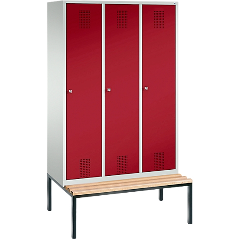 Taquilla con tres puertas rojas y un banco. Cada puerta tiene una pequeña rejilla de ventilación. El marco es blanco.