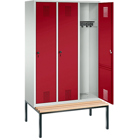 Taquilla con puertas rojas y una puerta abierta, con un banco.