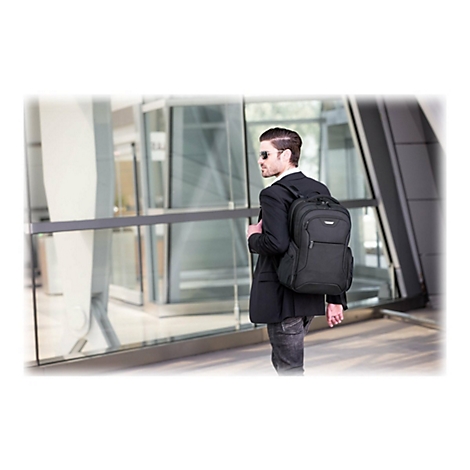 Mann mit Rucksack, Sonnenbrille und Anzug, der an einem sonnigen Tag vor einem modernen GebÃ¤ude steht.
