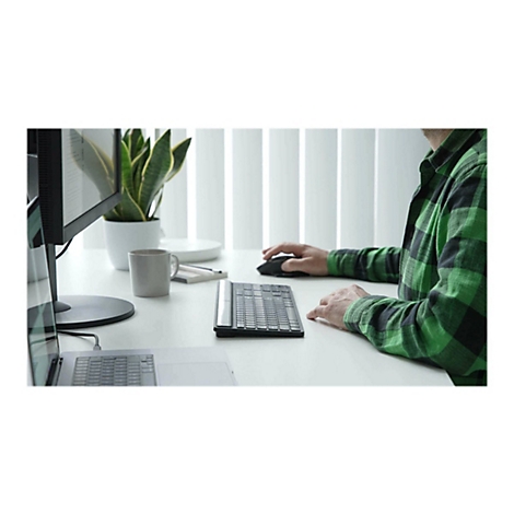 Personne utilisant un clavier et une souris au bureau. Moniteur, plante et tasse sont sur la table.