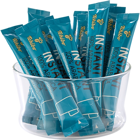 Mehrere türkisfarbene Sticks von Tchibo Instant Kaffee stecken in einer transparenten Glasschale.