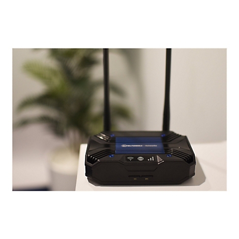 Ein schwarzer Router steht auf einem weiÃŸen Tisch. Auf der Oberseite des Routers befindet sich ein blaues Element mit weiÃŸer Schrift. Zwei Antennen ragen in die HÃ¶he.
