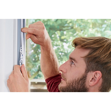 Ein Mann klebt Dichtung an ein Fenster. Der Blick des Mannes ist konzentriert. Die Hand des Mannes zeigt auf das Klebeband.