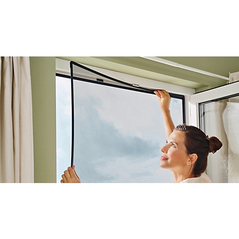 Une femme fixe une moustiquaire à une fenêtre. Le ciel est visible à travers la vitre.