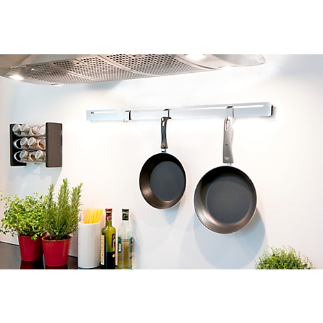 Two pans hang on a rail in a kitchen. Below are spices, herbs and oil bottles.