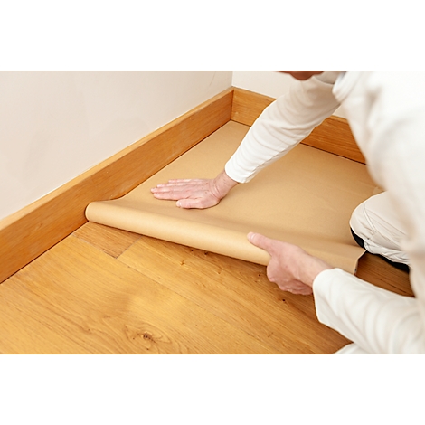 Eine Person rollt braunes Papier auf einem Holzboden aus, um diesen vor Farbe zu schützen.