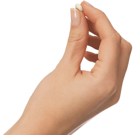 A hand holding a small, oval, cream-colored tablet between thumb and forefinger. Bright background.