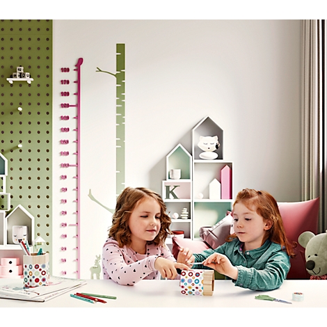 Two girls crafting at a table, with a height chart and house-shaped shelves in the background.