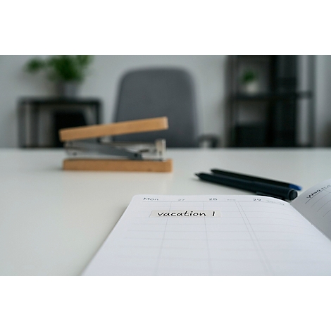 Close-up van een open notitieboek met het woord 'vakantie', daarnaast een nietmachine, pennen.