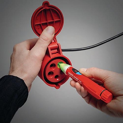 Une main tient une prise rouge dans laquelle est inséré un testeur de tension rouge. Câble noir visible.