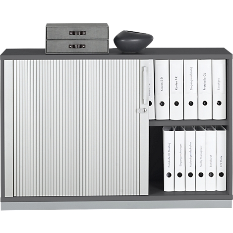 Grey filing cabinet with slatted door and white files. Grey boxes and a vase on the top.