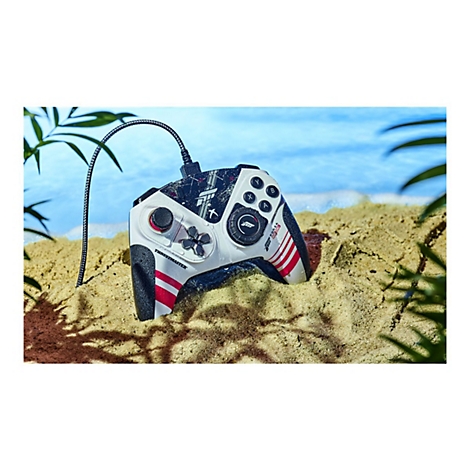 Ein weiß-schwarzer Gamecontroller, der auf Sand liegt, mit roter Markierung. Im Hintergrund ist das Meer.