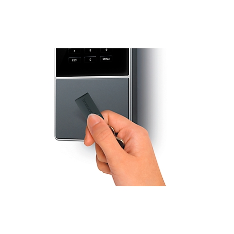 A hand holds a card in front of a gray card reader. Buttons and lettering can be seen in the upper part of the reader.