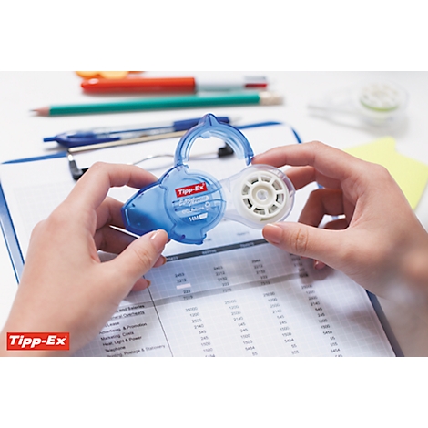 Hands holding a blue Tipp-Ex correction roller, lying on a clipboard with papers. Pens are in the background.