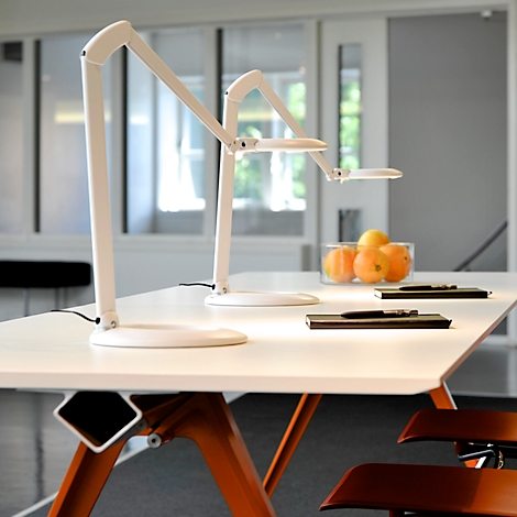 Zwei weiße Schreibtischlampen auf einem weißen Tisch. Im Hintergrund Obst und ein Stuhl.