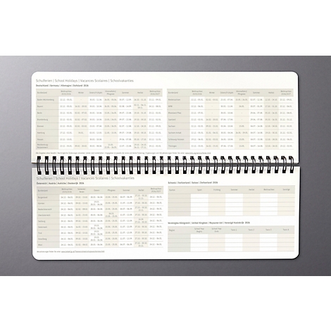 Geöffneter, gebundener Kalender, grauer Hintergrund. Beide Seiten zeigen Tabellen mit Informationen und Uhrzeiten.