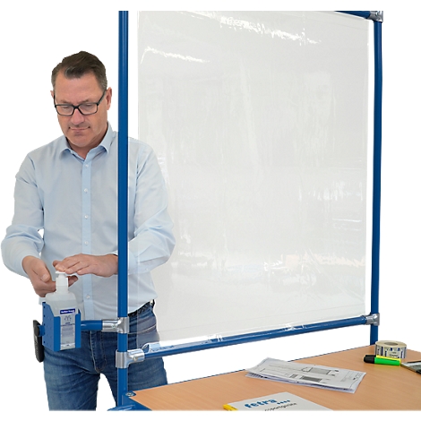 Ein Mann mit Brille an einer Trennwand, benutzt Desinfektionsmittel.