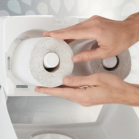 Handen plaatsen toiletpapierrollen in een witte dispenser. Eén rol zit al op zijn plaats.
