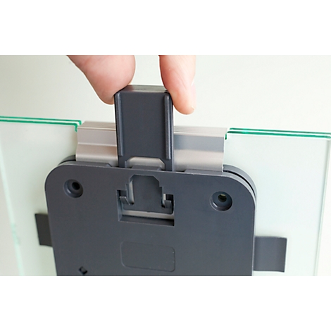 Close-up of a hand attaching a gray plastic closure to a glass picture. In detail, the bracket is being mounted.