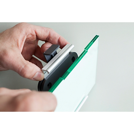 A hand holds a bracket for a glass plate with a green edge. The product is being assembled in the hand.