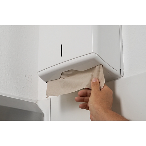 Hand pulling a paper towel from white dispenser on white wall.
